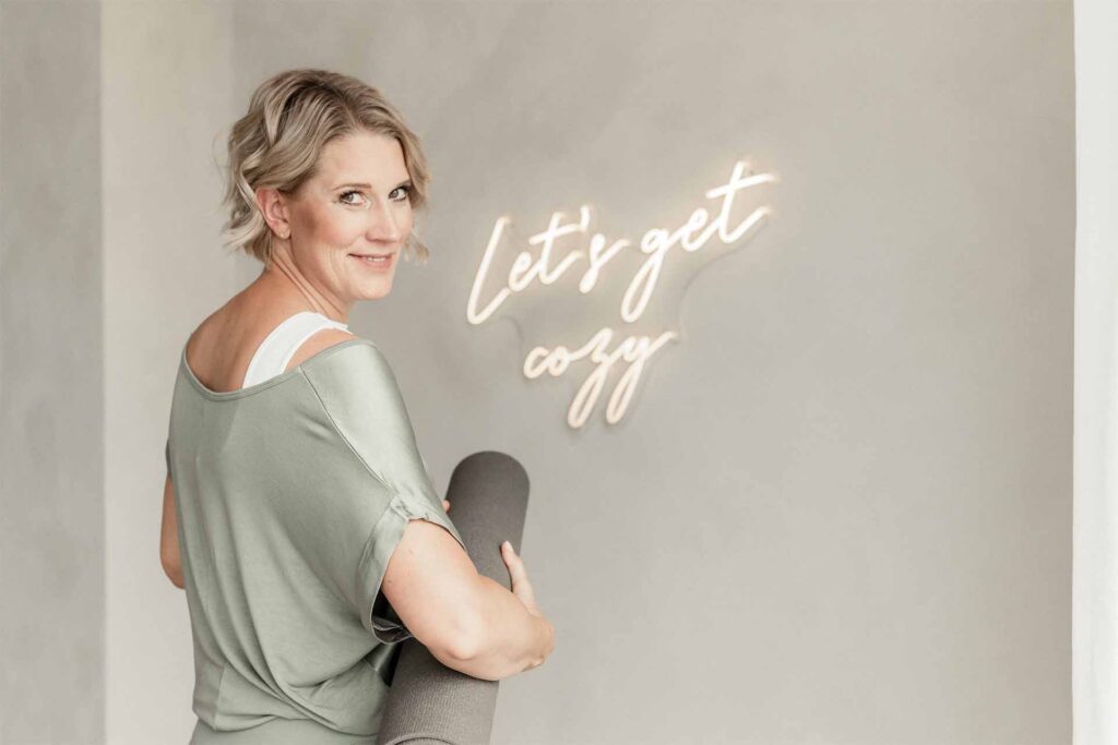 Was ist Achtsamkeit/ Mindfulness?: Julia Jäger lächelt über die Schulter und hält eine Yogamatte unter dem Arm